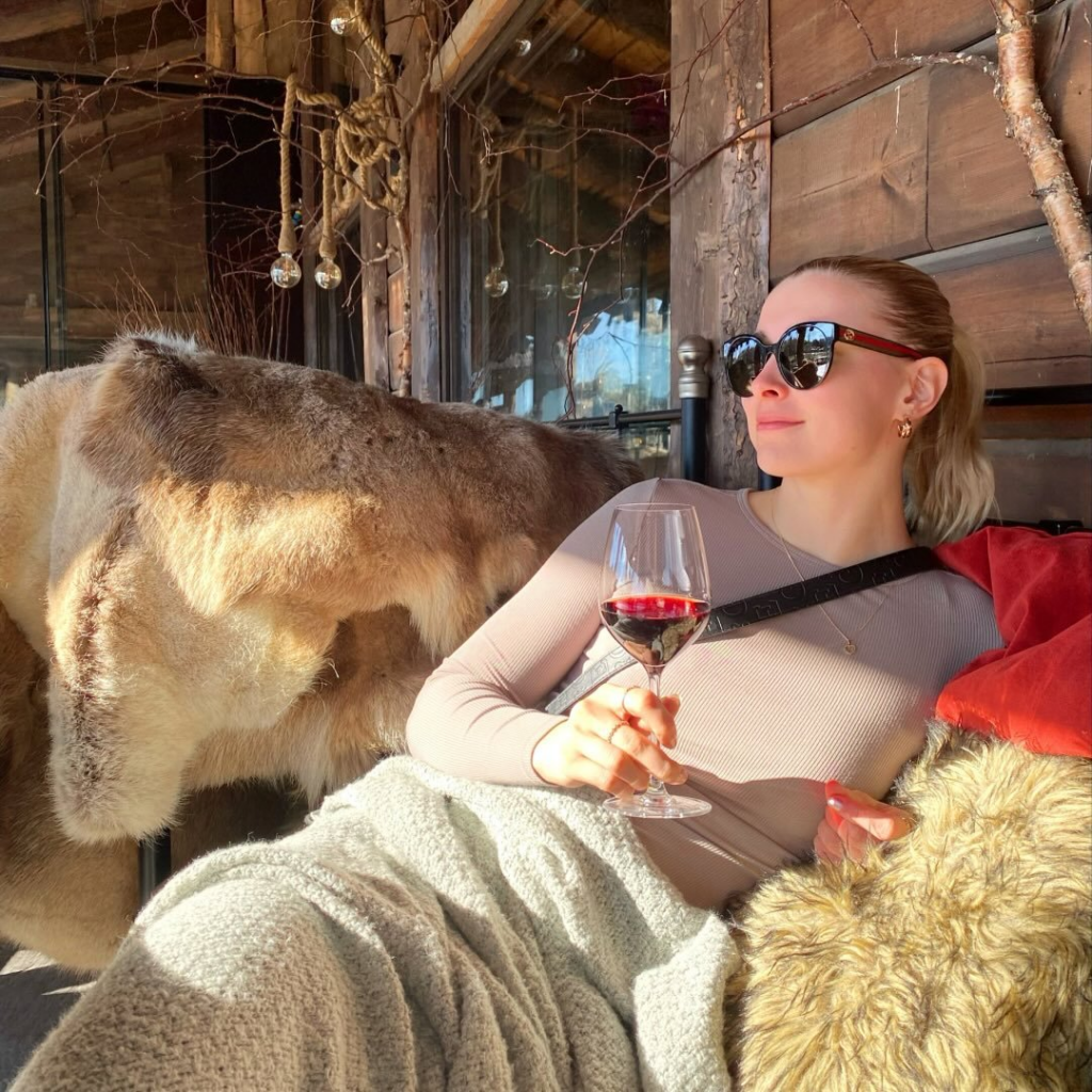 Sara Taavitsainen nauttii aurinkoisesta hetkestä terassilla pitäen viinilasia kädessään.
